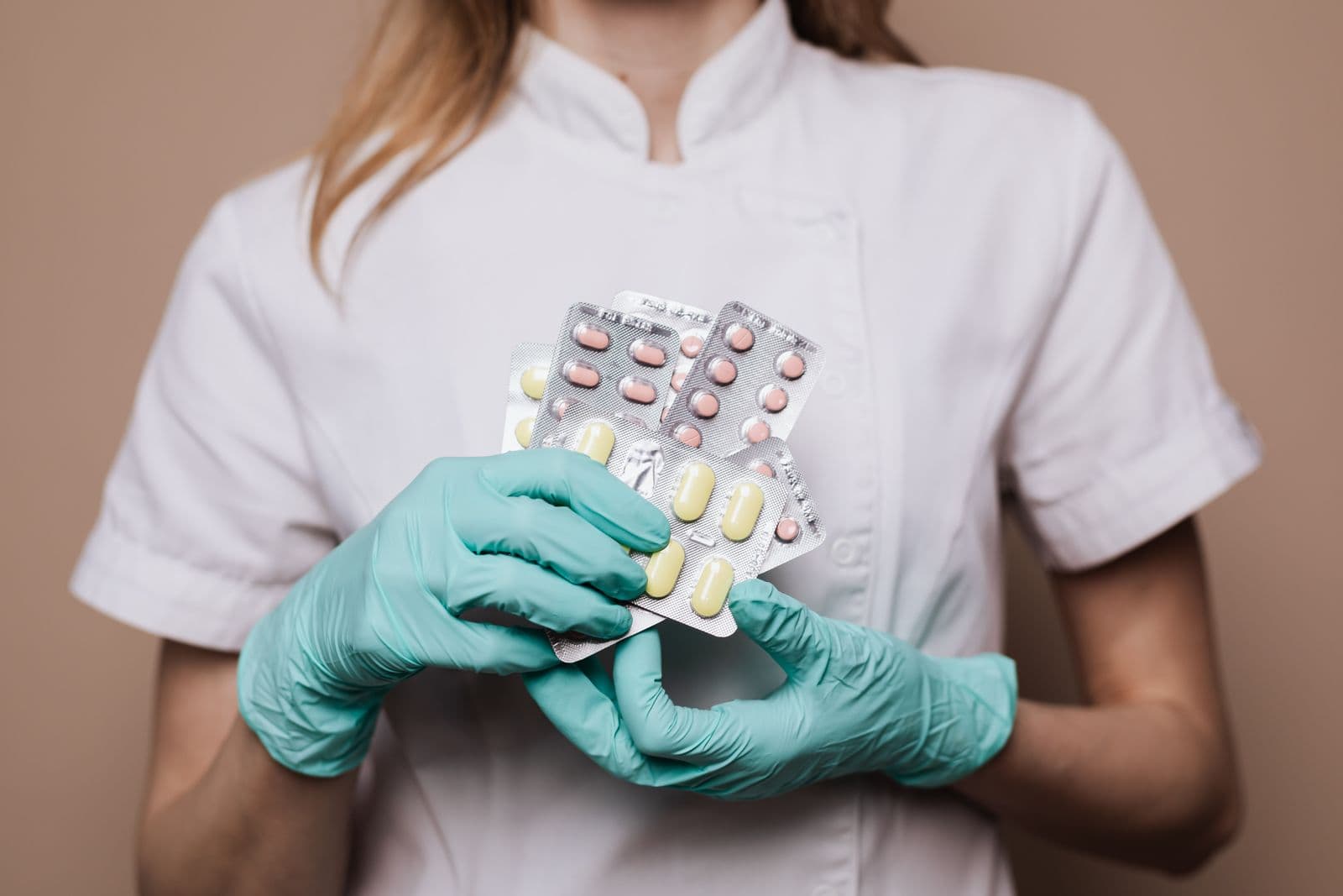 Mãos com luvas cirúrgicas seguram cartelas de comprimidos coloridos