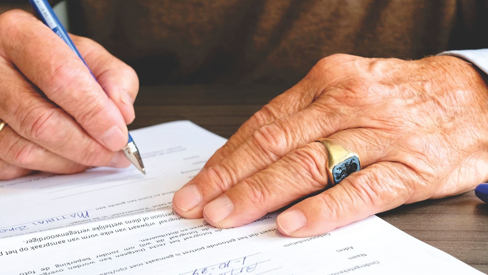 Close-up de mãos assinando um documento formal com caneta, uma das mãos com anel