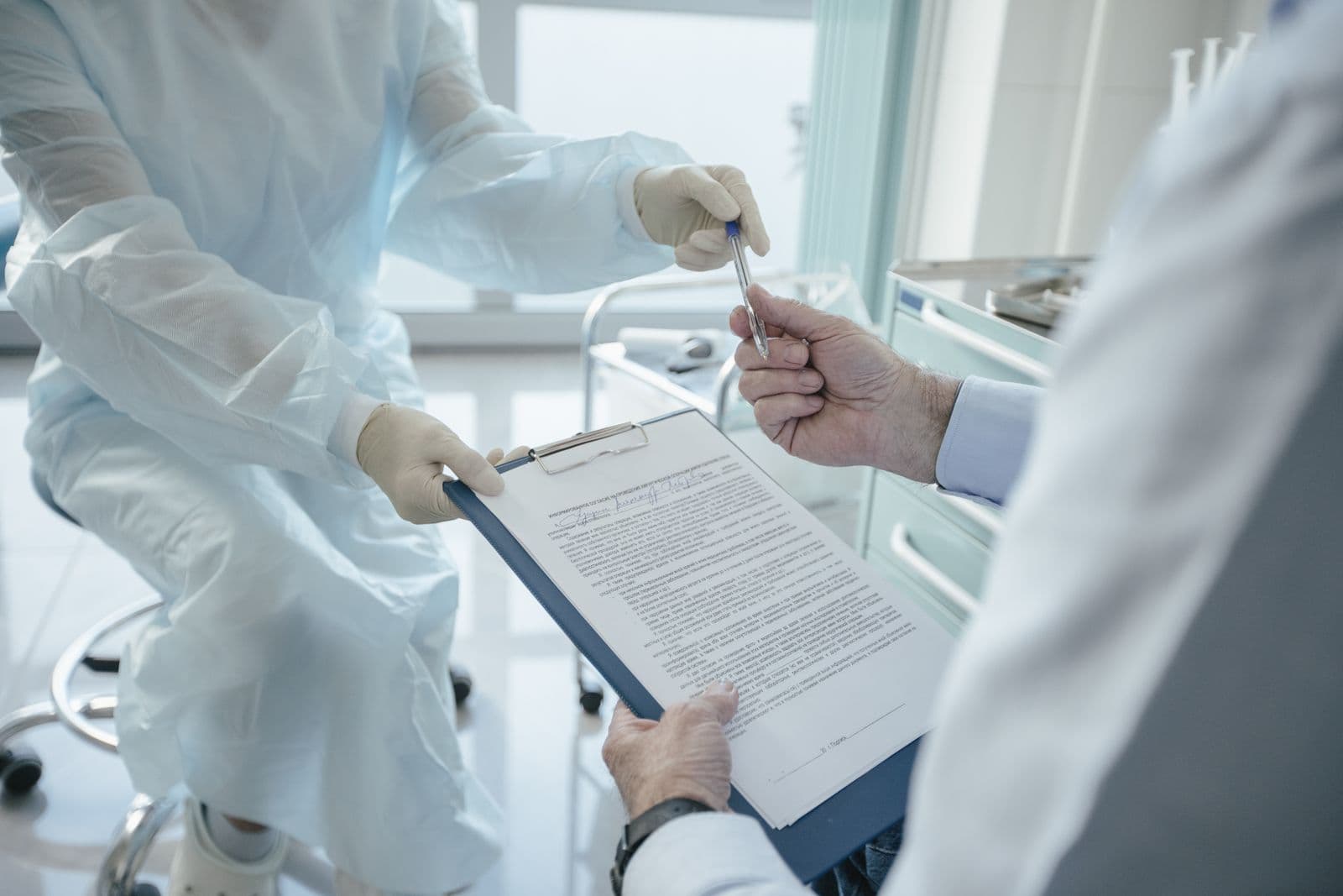 Médico entrega uma prancheta com um termo de consentimento para o paciente assinar em um consultório